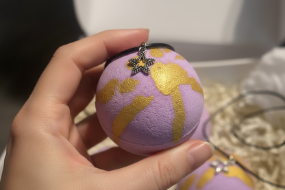 Hand holding golden grape bath bomb with charm necklace