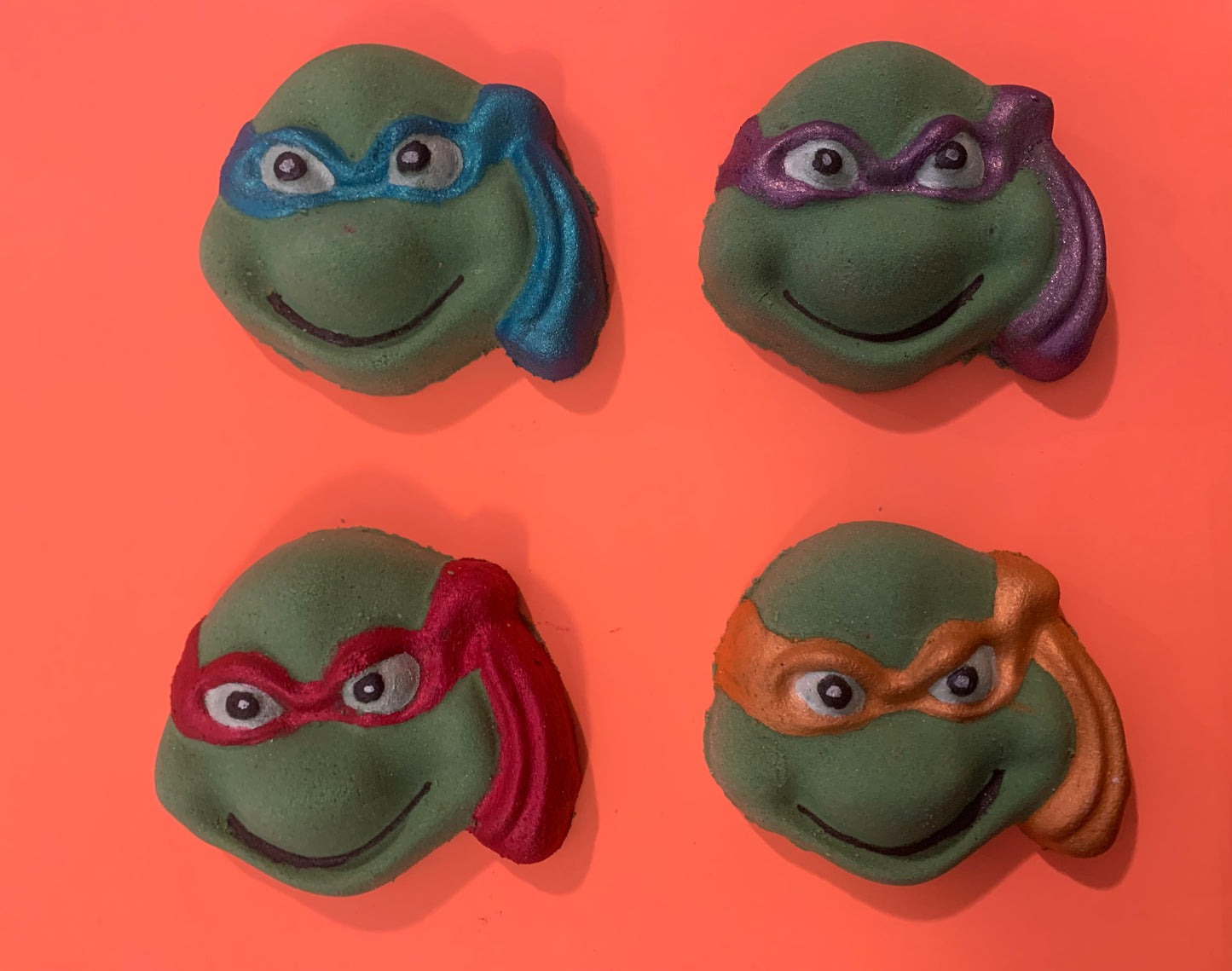 Four green turtle masks with colored eye masks on an orange background